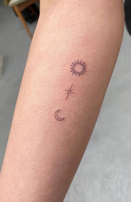 Minimalist tattoo with sun, star, and crescent moon symbols on forearm