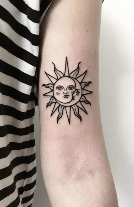 Sun and moon face tattoo with detailed rays on the upper arm