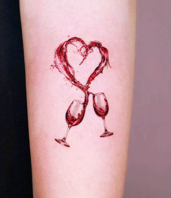 Wine glasses clinking with red wine splashing into a heart shape tattoo on forearm