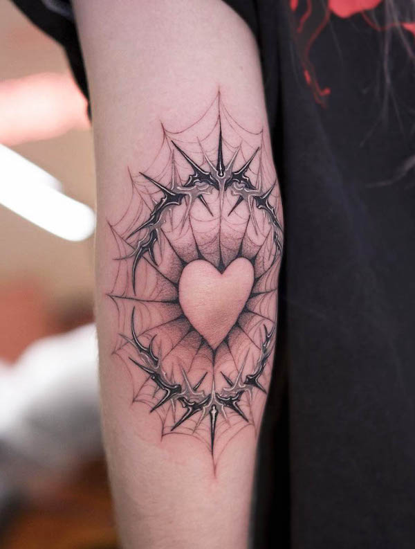 Heart tattoo surrounded by thorns and web design with black and gray shading on upper arm