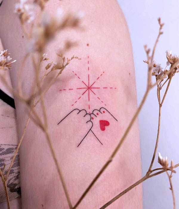 Pinky promise tattoo with red heart and starburst design on upper arm