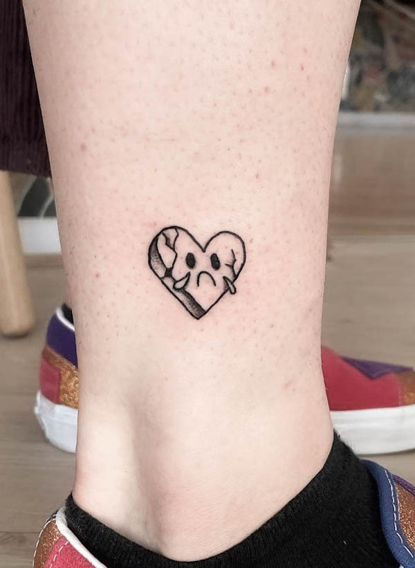 Small sad face broken heart tattoo in black ink on lower leg