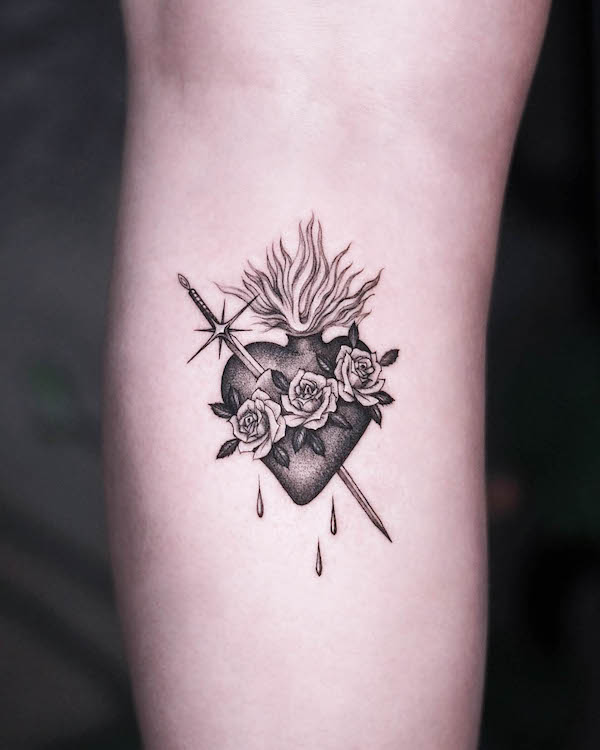 Sacred Heart tattoo with roses, sword, and flames in black and gray ink on arm.