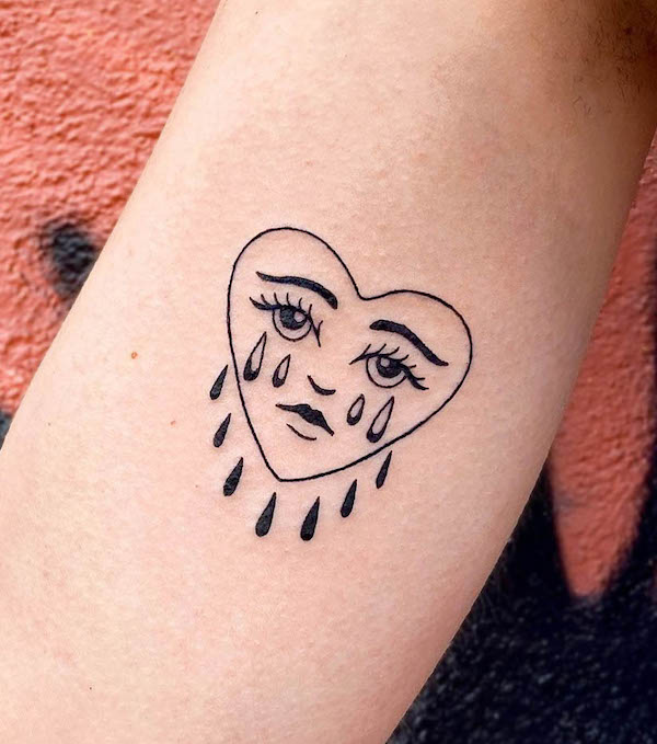 Minimalistic crying heart face tattoo in black ink on forearm