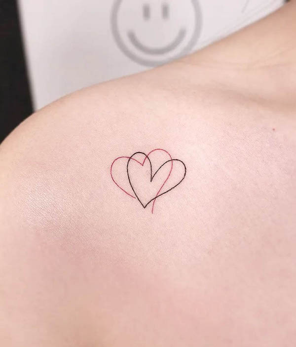 Minimalistic interlocking hearts outline tattoo in black and red ink on upper shoulder.