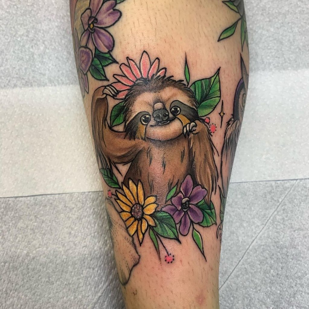 Adorable sloth tattoo surrounded by vibrant flowers and green leaves with colorful details