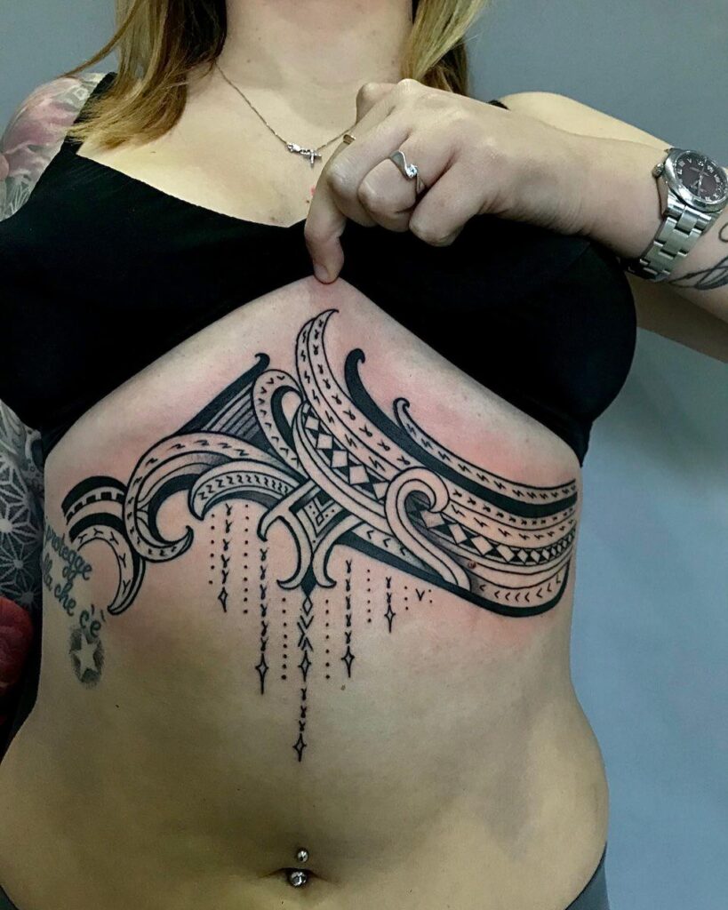 Under-breast tattoo with bold Polynesian-inspired patterns and intricate hanging geometric details