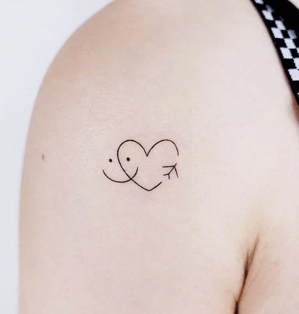 Minimalist smiling heart tattoo with black linework on upper arm