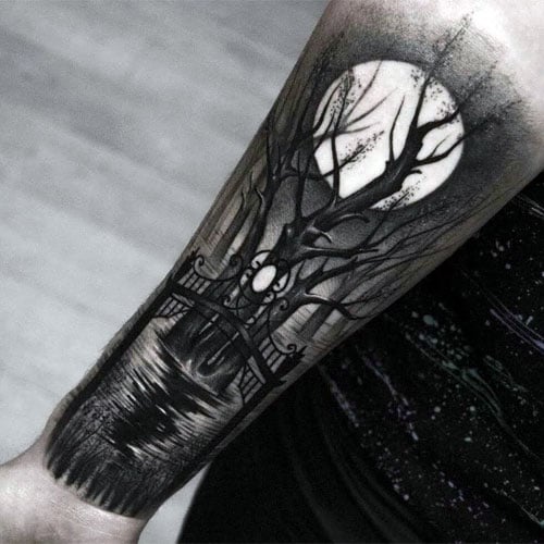 A black and white forearm tattoo featuring a dark forest with a full moon illuminating bare trees and a reflection over a body of water