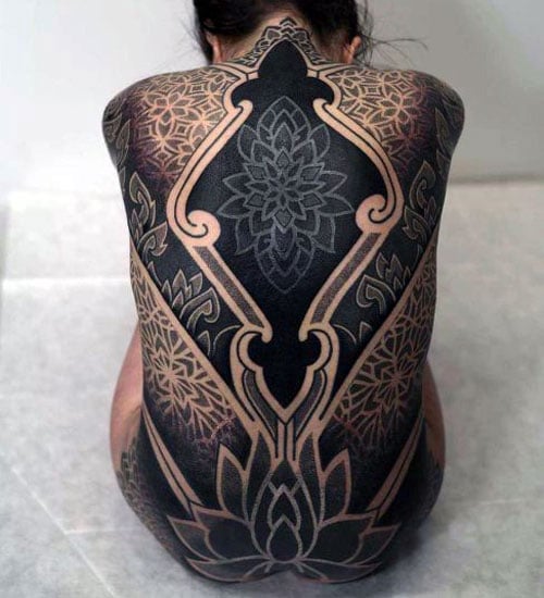 A full-back blackout tattoo featuring intricate geometric and mandala patterns with negative space creating detailed designs across the entire back