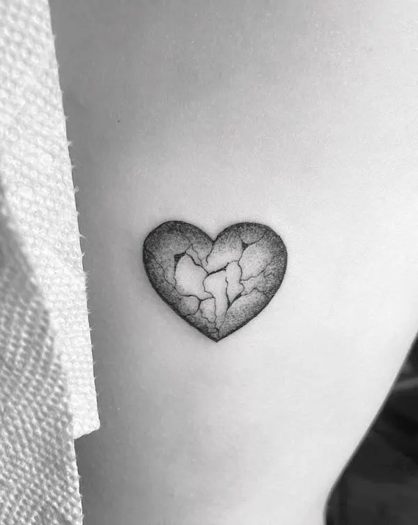 Cracked heart tattoo in black and gray shading symbolizing resilience and emotional endurance