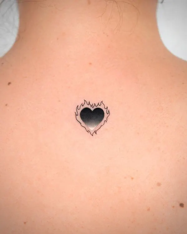 Black heart with flame outline tattoo on the back, symbolizing passion, transformation, and resilience