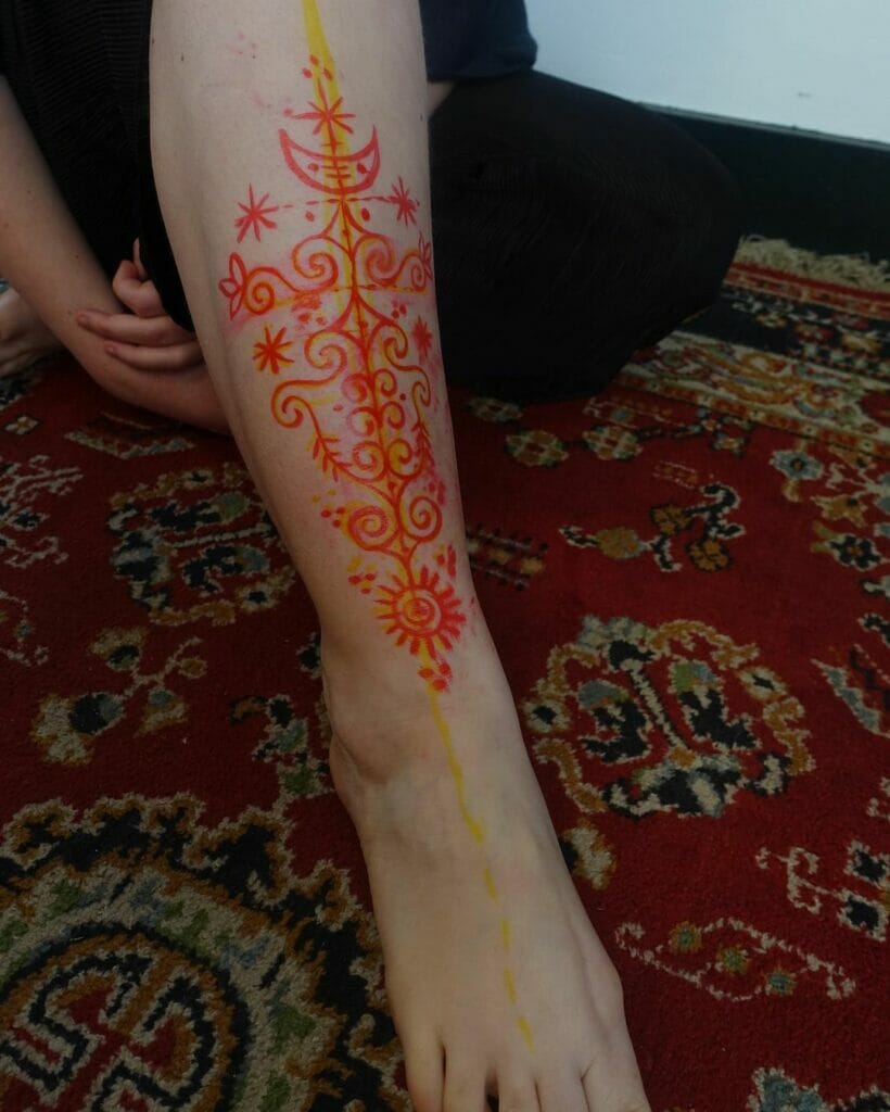 Vibrant abstract leg tattoo in red and yellow with intricate swirling patterns and celestial elements