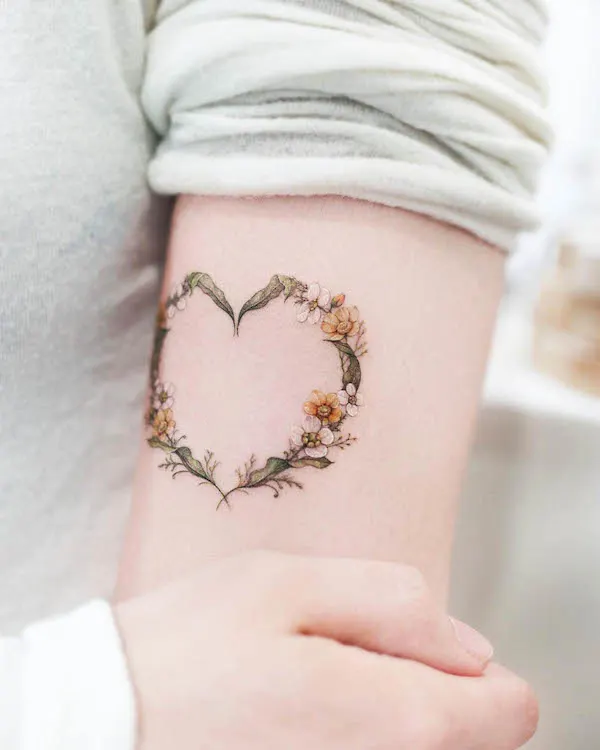 Delicate floral heart tattoo with small flowers and green leaves in soft colors