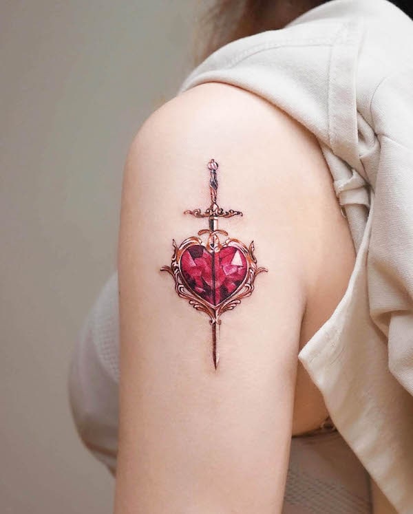 Ornate heart tattoo with sword piercing through it, gemstone design in red on upper arm.