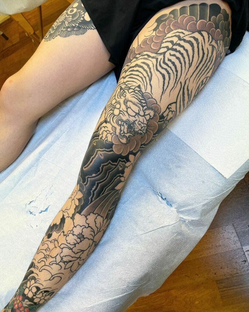 Japanese tiger leg sleeve tattoo with intricate black and beige details and traditional floral elements