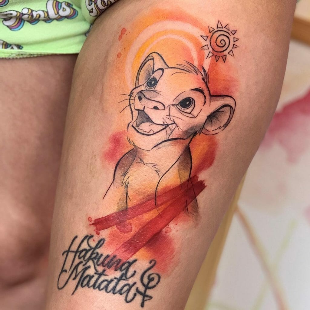 Thigh tattoo of young Simba with vibrant watercolor background and "Hakuna Matata" text, symbolizing joy, freedom, and a carefree spirit.