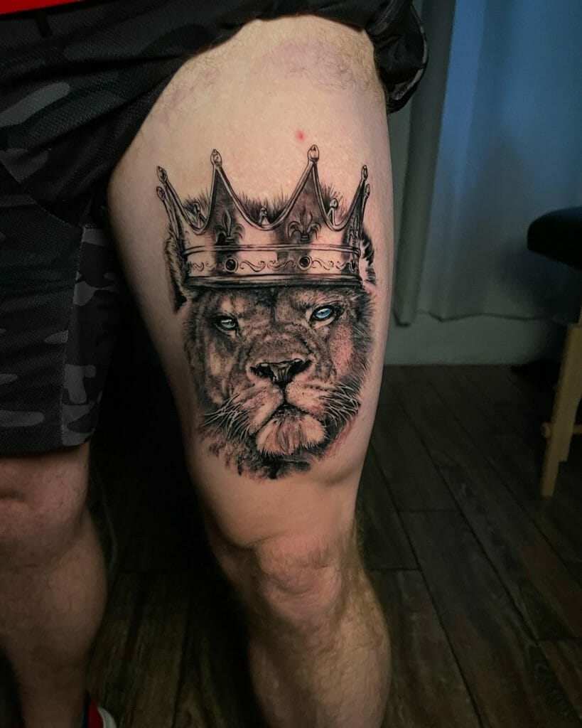 Thigh tattoo of a lion with a detailed crown and piercing blue eyes, symbolizing strength, royalty, and authority.