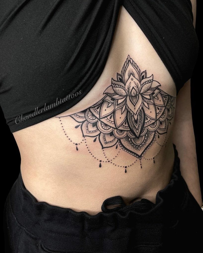 Under-breast tattoo featuring a detailed lotus and mandala design with intricate line work and dotted hanging accents