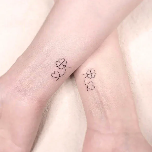 Matching clover and heart tattoos with minimalist line design on wrists symbolizing love and luck