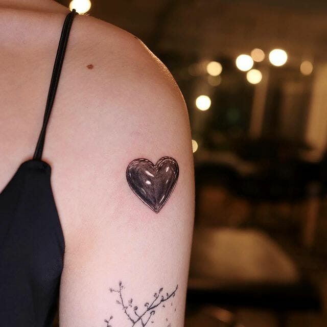 Realistic shaded heart tattoo with black and gray shading on upper arm