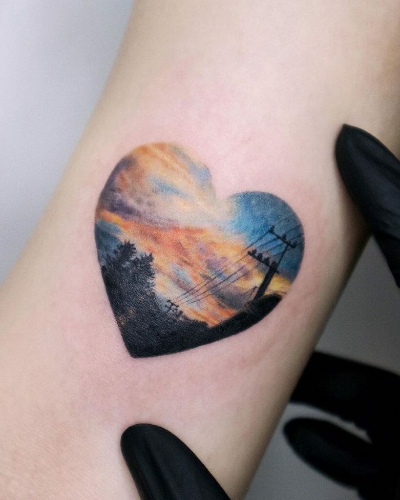 Heart-shaped sunset landscape tattoo with vibrant colors on inner arm