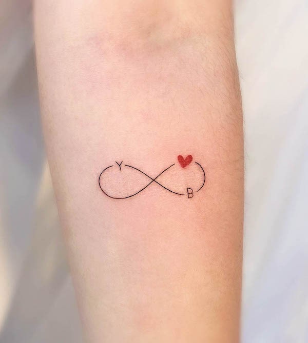 Infinity tattoo with red heart and initials 'Y' and 'B' in black linework on arm