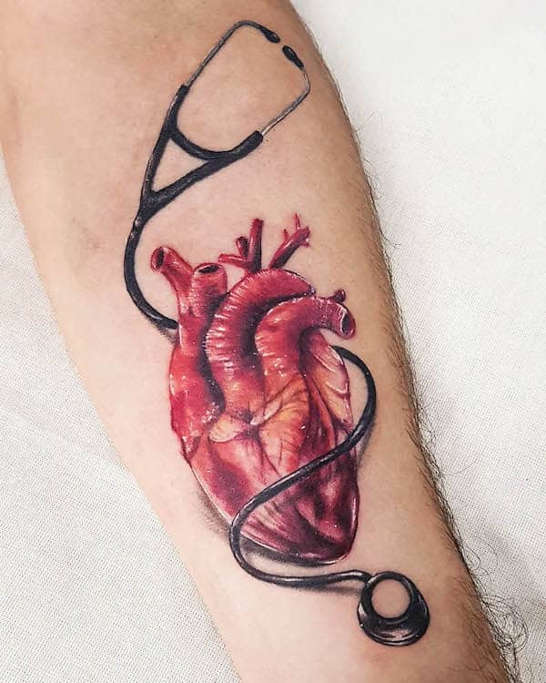 Realistic anatomical heart tattoo with stethoscope in black and red on forearm