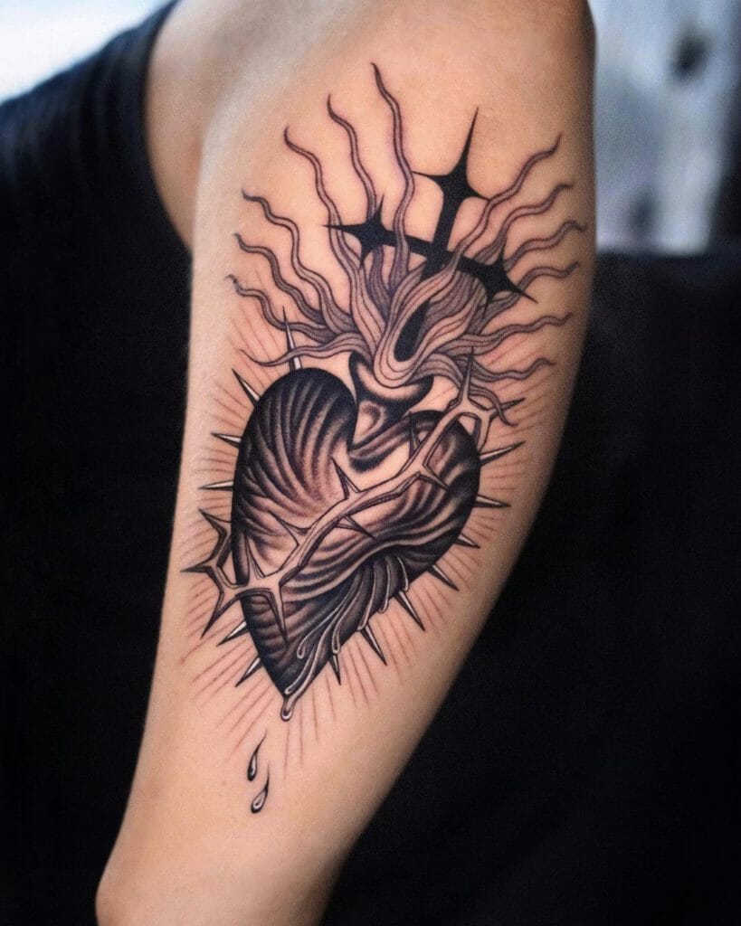 Flaming sacred heart tattoo with crown of thorns on upper arm, black and gray shading.