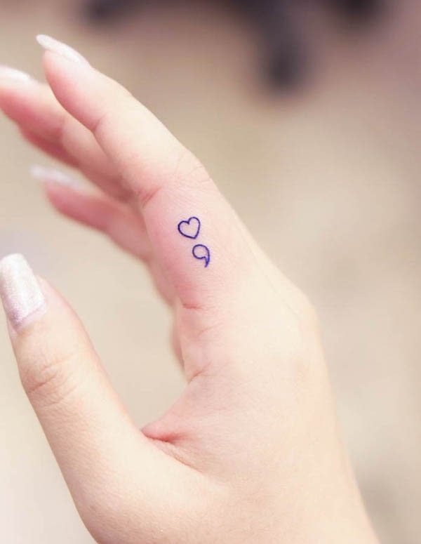 Minimalist heart and comma tattoo in blue linework on finger