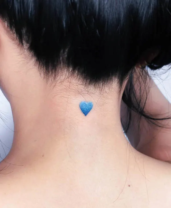 Small blue heart tattoo on the nape of the neck, symbolizing serenity, loyalty, and calm emotional strength.