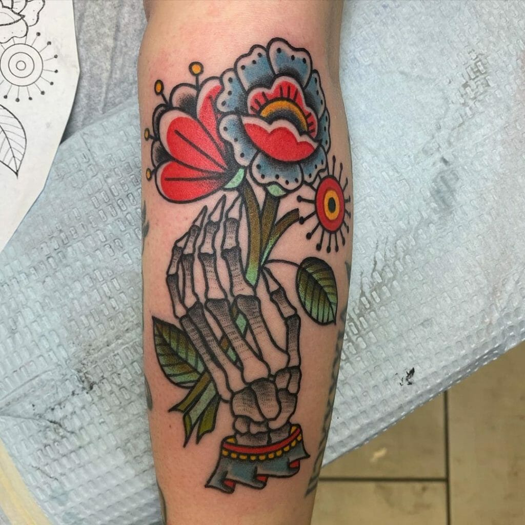 Traditional skeleton hand tattoo holding vibrant flowers with bold colors and intricate details