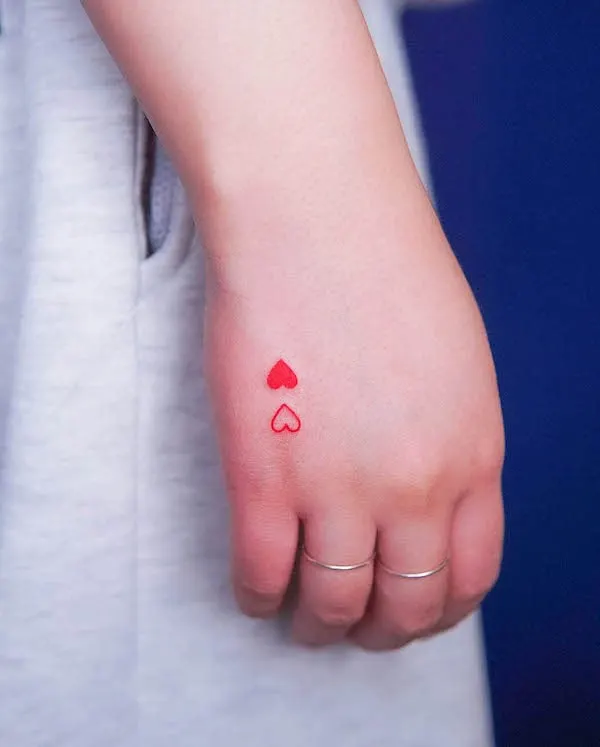 Double red heart tattoo on the side of the hand, symbolizing love and connection