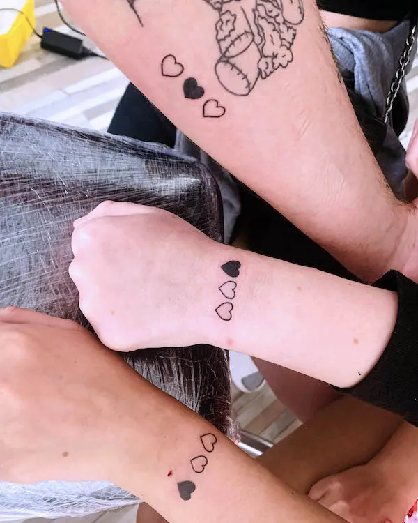 Matching tattoos of three heart outlines with one filled heart on wrists and forearms