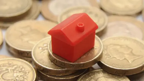 PA A picture of a red model house from the board game Monopoly sat on a pile of pound coins