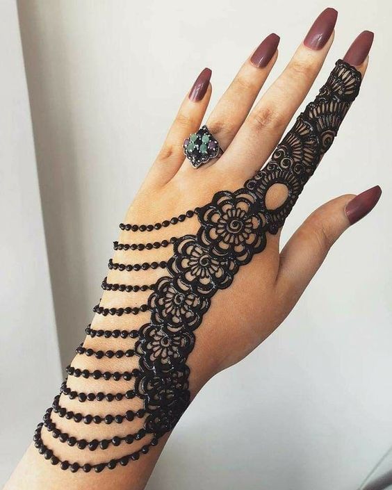 Black lace-inspired Mehndi design on the backhand with floral motifs and cascading beaded lines extending from the wrist to the finger