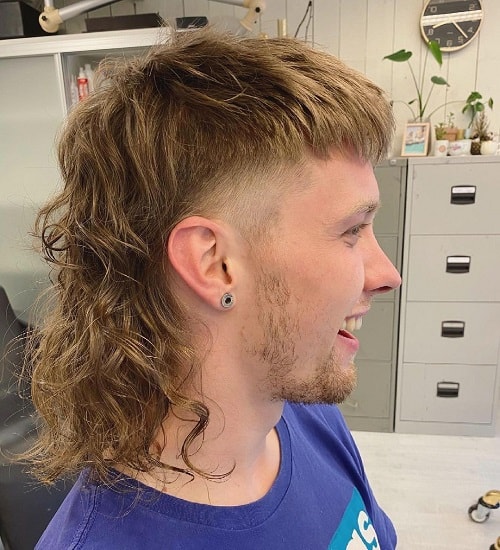 Side view of a man with a textured mullet haircut featuring curly long back hair and tapered sides.