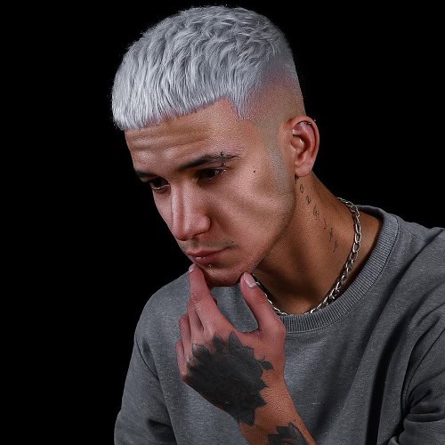 Man with a silver crew cut hairstyle and a fade, wearing a gray shirt, and showing tattoos on his hand and neck.