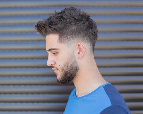 Man with a textured crew cut hairstyle and a fade, wearing a blue t-shirt.