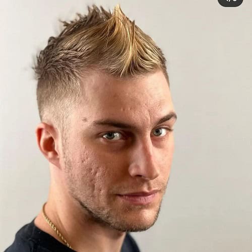 Man with a spiky crew cut hairstyle featuring blonde highlights and a fade, wearing a black shirt