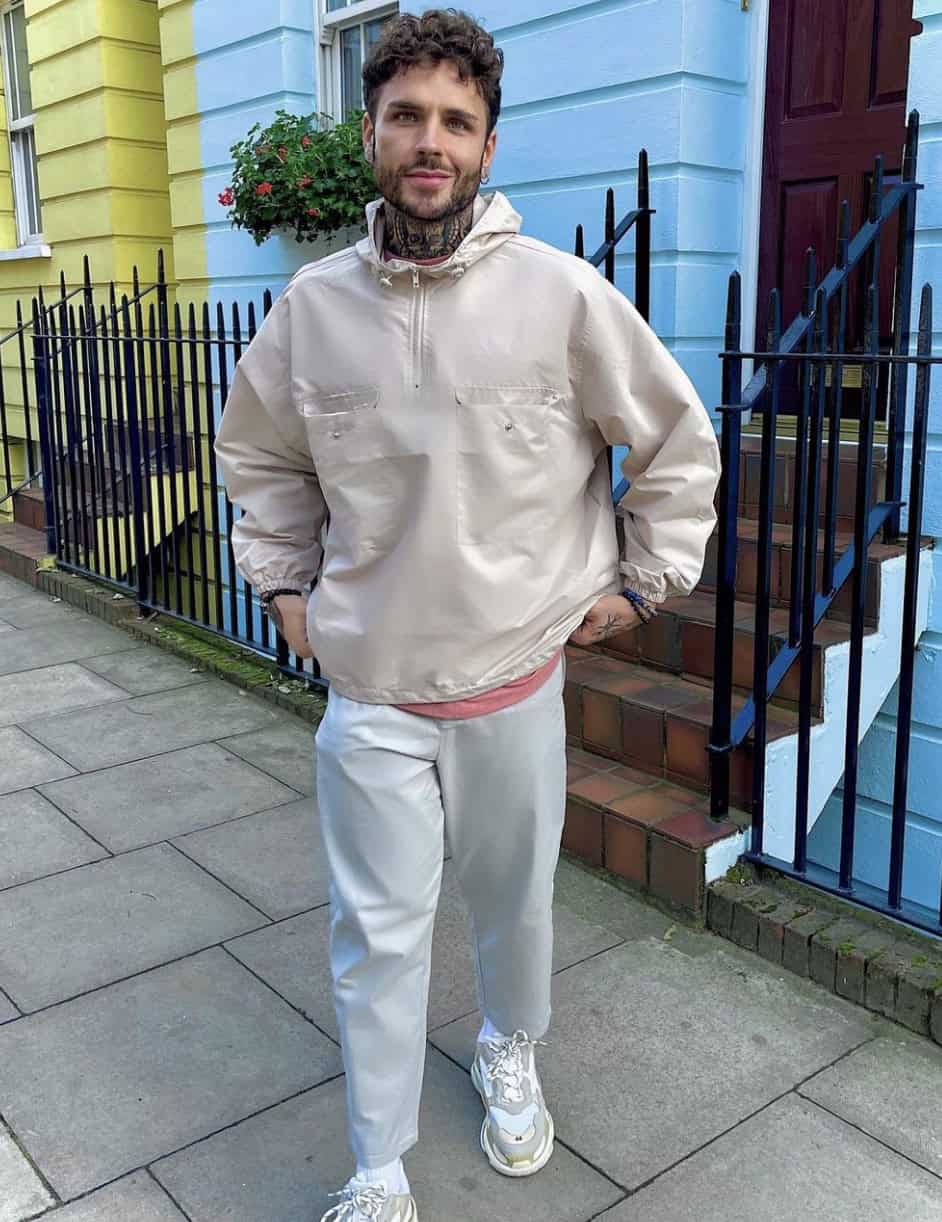 Man with a crew cut hairstyle, standing in casual outdoor attire with a jacket and white pants.