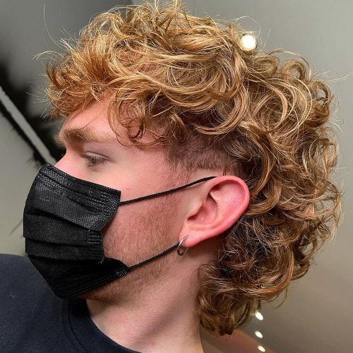 Side view of a man with a curly mullet and a skin fade, showcasing voluminous curls on top and a faded undercut.