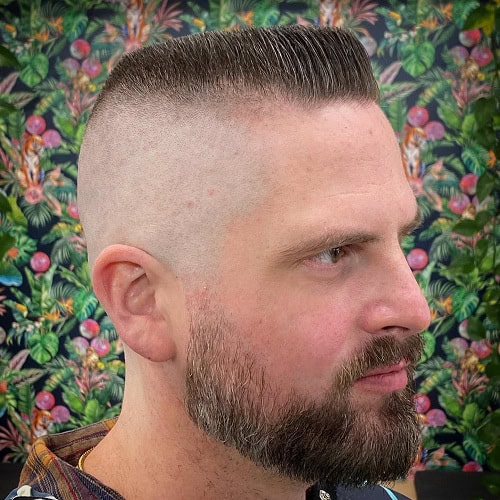 Man with a high and tight crew cut hairstyle featuring a sharp fade and a full beard, wearing a patterned shirt.