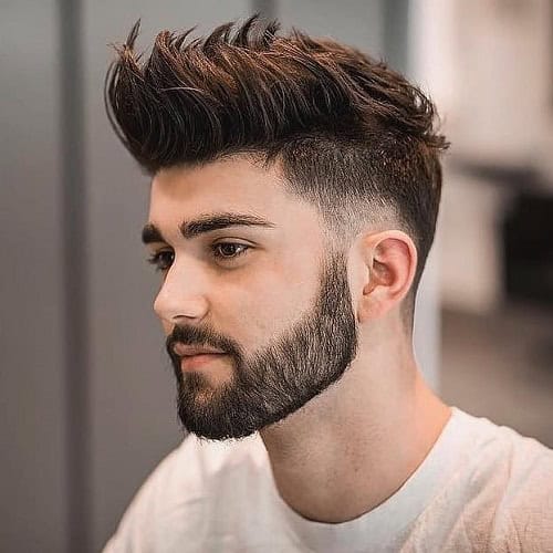 Man with a spiked crew cut hairstyle featuring a fade and a full beard, wearing a white t-shirt.