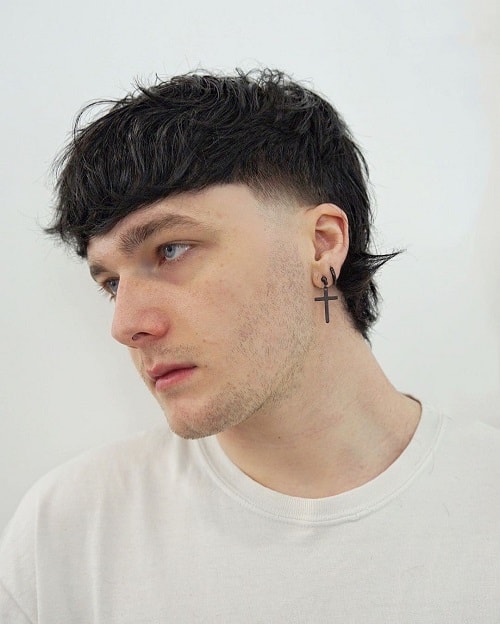 Side view of a man with a textured mullet haircut, featuring a tapered fade and choppy layers at the top and back