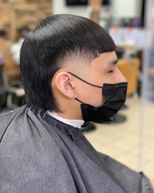 Side view of a man with a straight-edge mullet and skin fade, featuring a sharp fringe and sleek long back