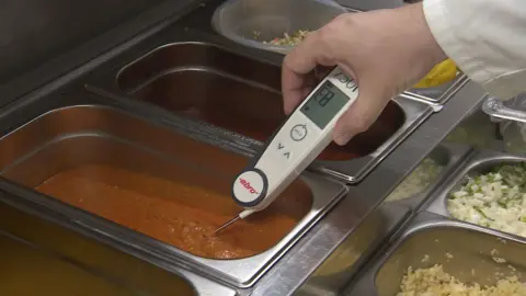 A food thermometer being used to take the temperature of s container of brown liquid