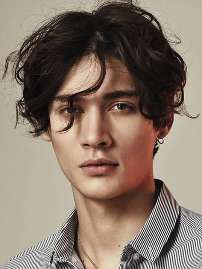 Young man with a textured Eboy haircut, featuring loose waves and a defined middle part, wearing a striped shirt.