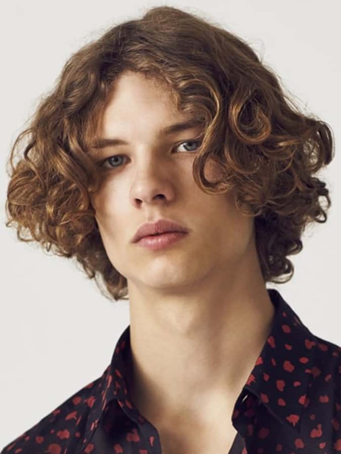 Young man with a curly Eboy haircut, featuring voluminous curls and a middle part, wearing a patterned shirt.