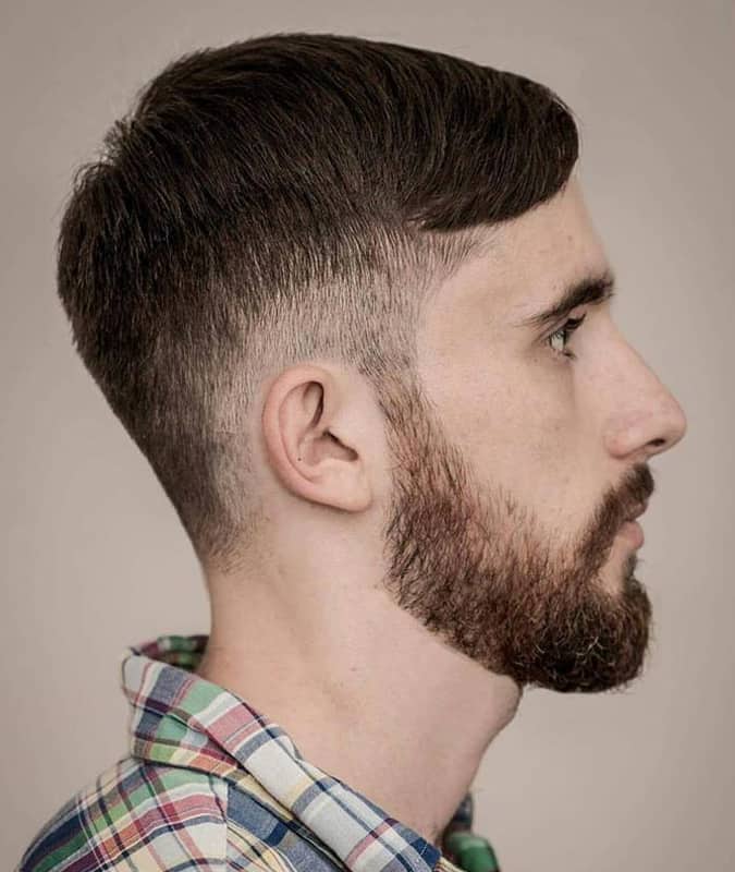 Profile of a man with a low drop fade haircut, short comb over, and neatly trimmed beard.